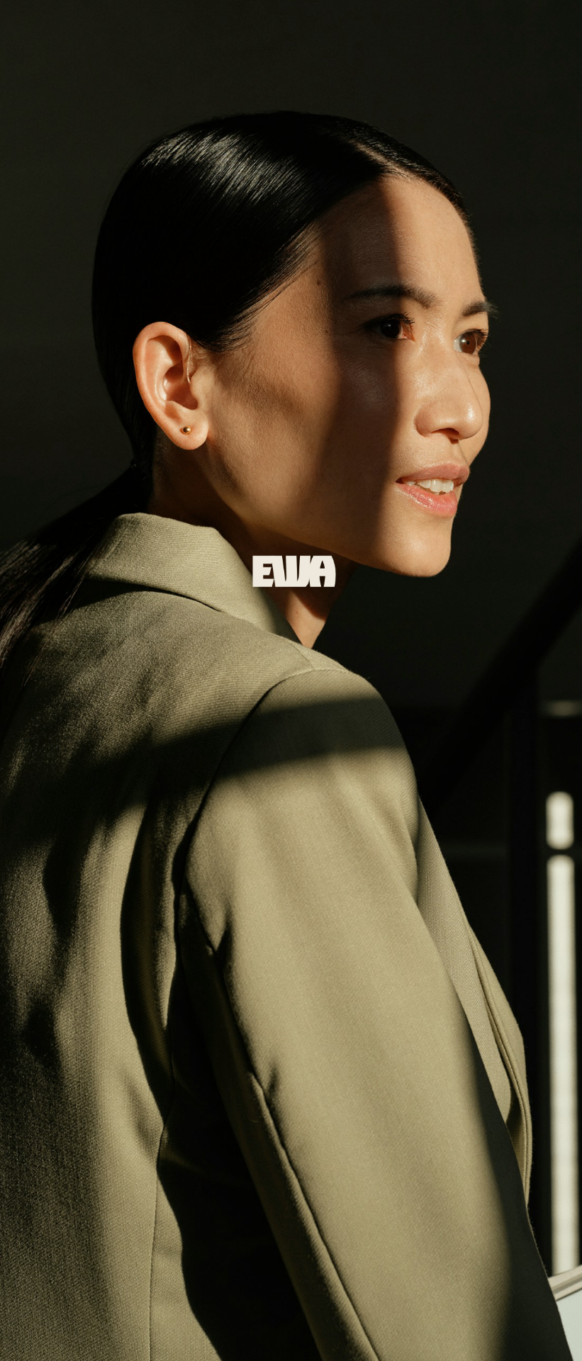 Woman in a green blazer holding her phone, with the EWA logo behind her